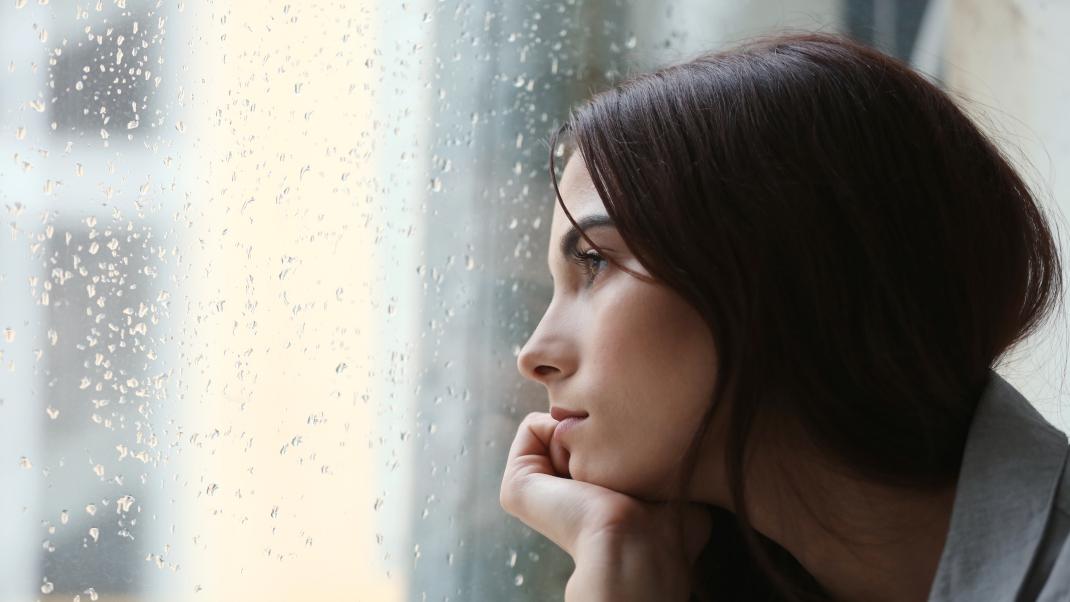 Μια μελαχρινή γυναίκα κοιτάζει το παράθυρο που βρέχει 