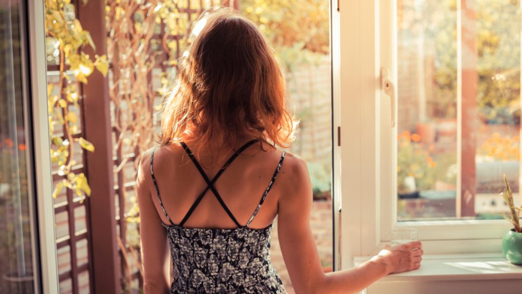 Μια γυναίκα κοιτάει από το ανοιχτό παράθυρο, Φωτογραφία: Shutterstock/By Lolostock