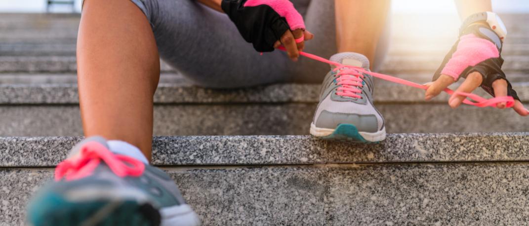 Γυναίκα καθισμένη σε σκαλιά δένει τα αθλητικά της παπούτσια με ροζ κορδόνια