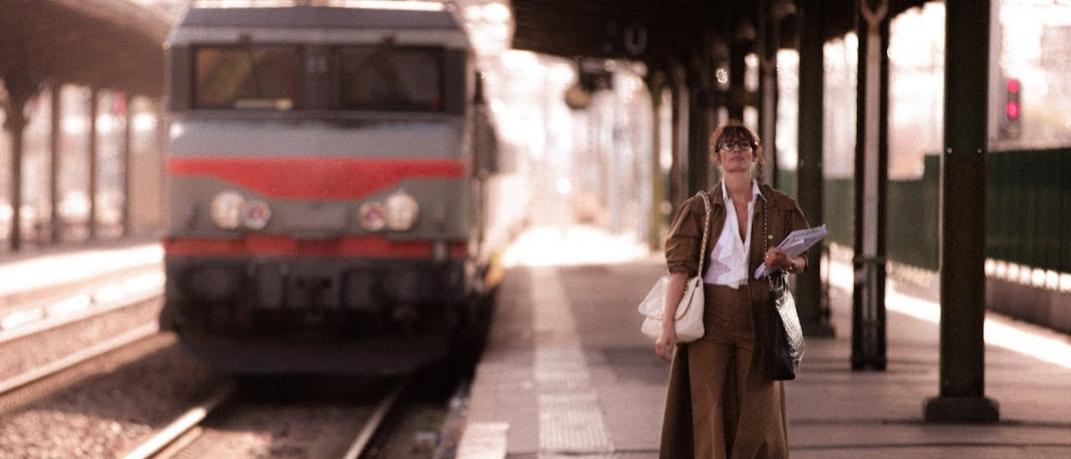 γυναίκα περπατά με καμπαρντίνα σε σταθμό τρένου