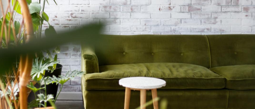 Πράσινος καναπές και ρατάν φωτιστικό, φυτά και τοίχος με τούβλα 