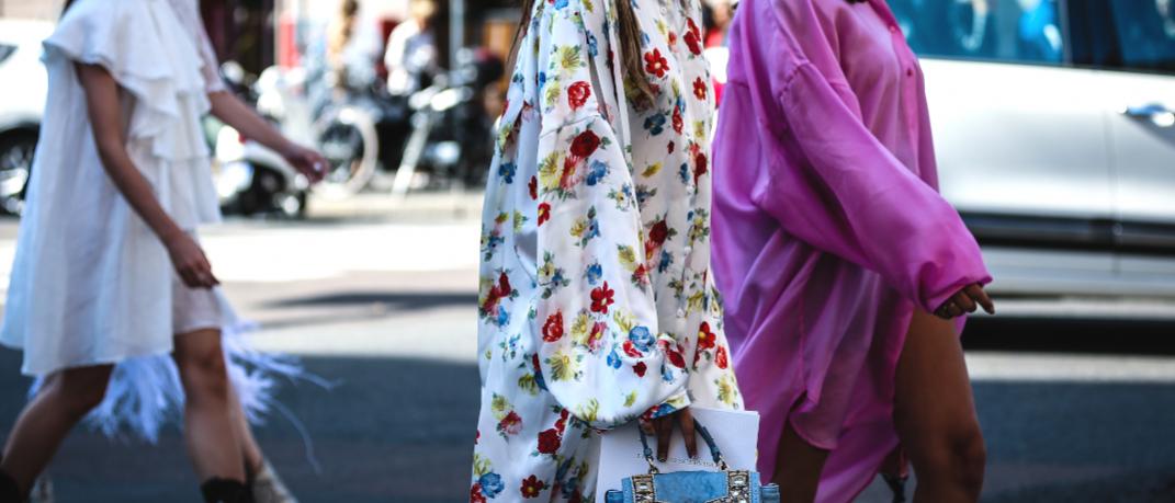 γυναίκα με φλοράλ φόρεμα και τσάντα περπατά στην εβδομάδα μόδας