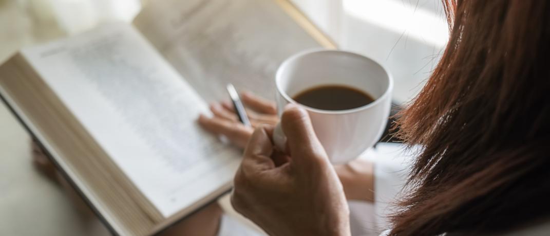 Γυναίκα κρατάει ένα φλιτζάνι καφέ και διαβάζει το βιβλίο της