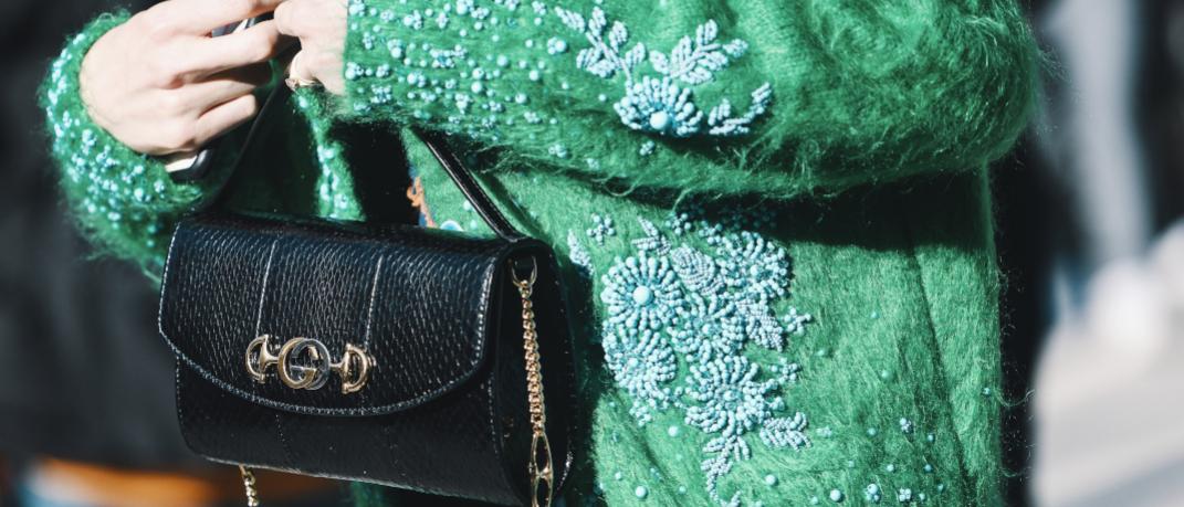 γυναίκα με πράσινη ζακέτα και τσάντα περπατά στην εβδομάδα μόδας