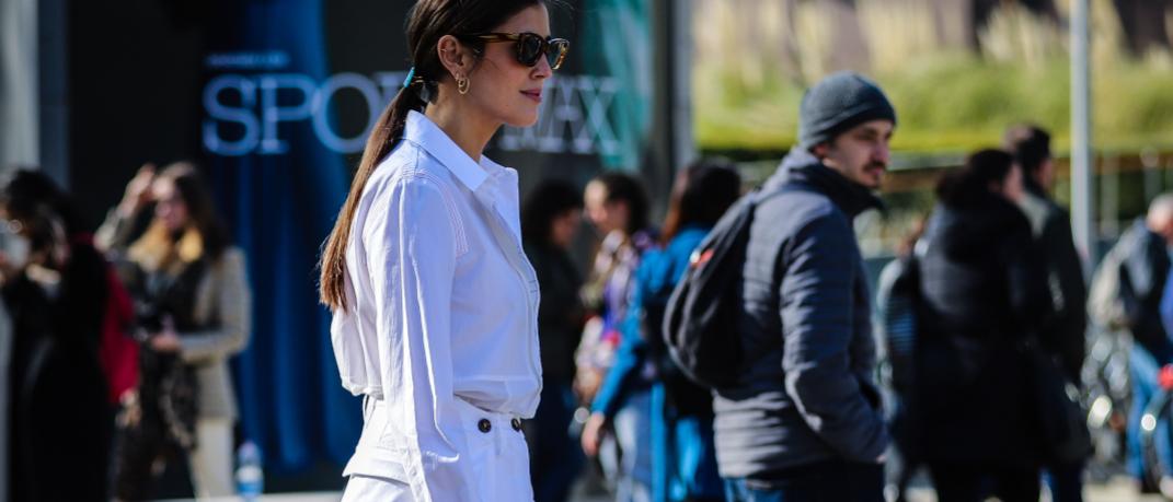 γυναίκα με λευκά ρούχα και γυαλιά ηλίου περπατά στο δρόμο