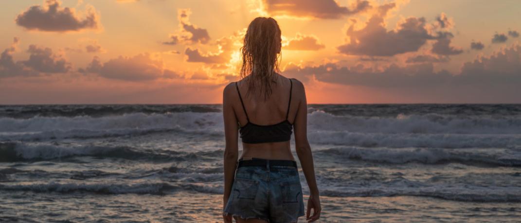 Γυναίκα απολαμβάνει ηλιοβασίλεμα σε παραλία 