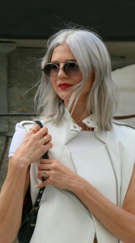 νεαρή γυναίκα με λευκή μπλούζα, μαύρη τσάντα, γυαλιά και γκρίζα μαλλιά