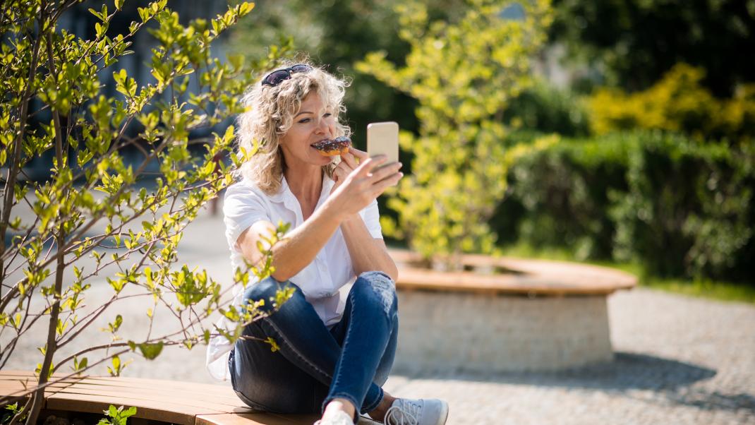 Μια γυναίκα είναι στο πάρκο και τρώει ντόνατ, βγάζοντας selfie