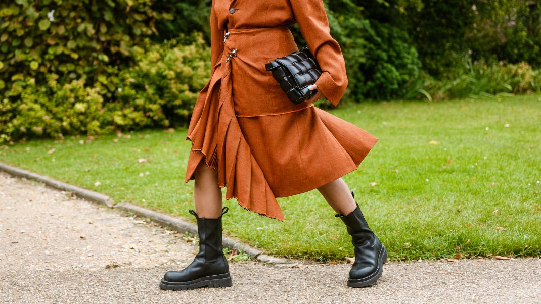 γυναίκα με φούστα και μπότες περπατά σε πάρκο στην εβδομάδα μόδας