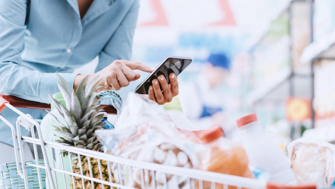 Γυναίκα κρατά κινητό πάνω από το καρότσι του σούπερμαρκετ 
