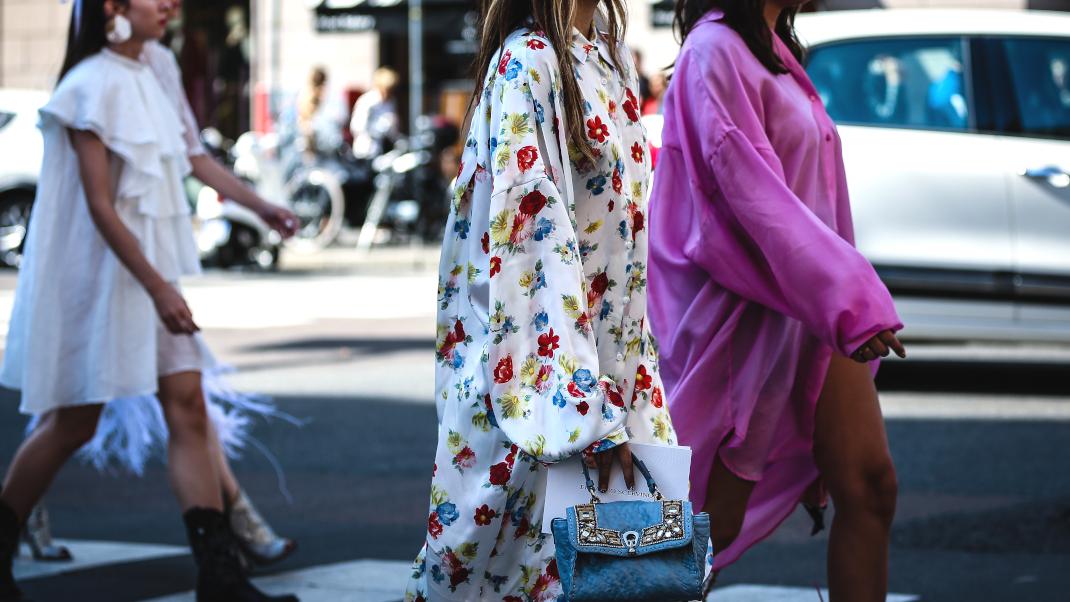 γυναίκα με φλοράλ φόρεμα και τσάντα περπατά στην εβδομάδα μόδας
