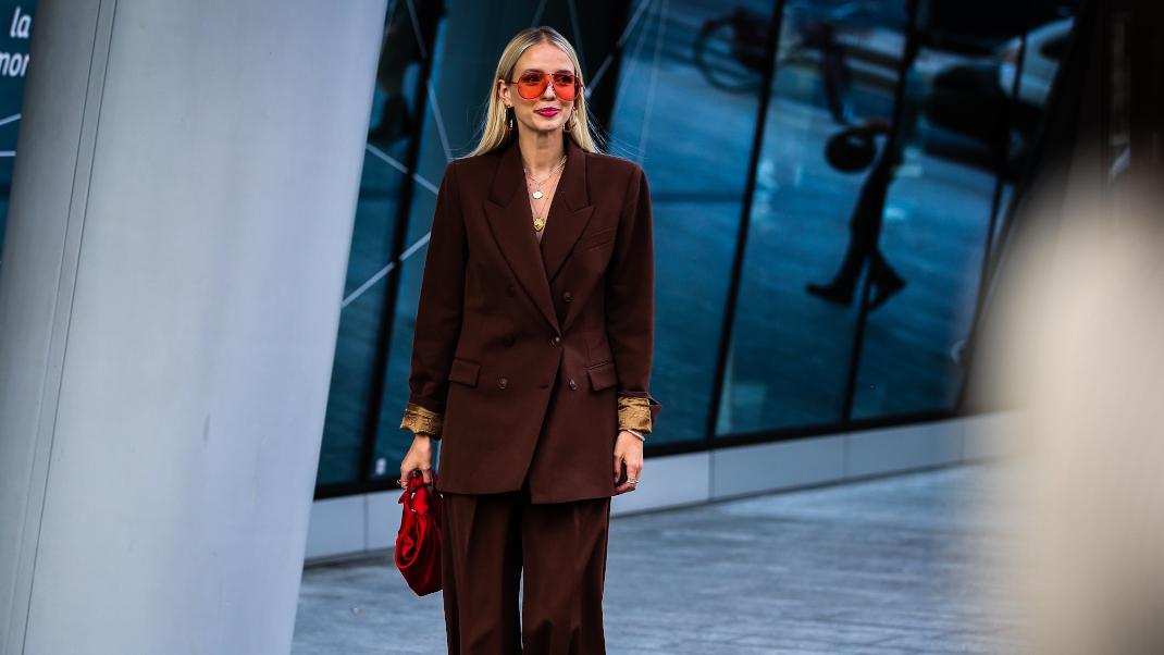 γυναίκα με κοστούμι και γυαλιά ηλίου περπατά στην εβδομάδα μόδας