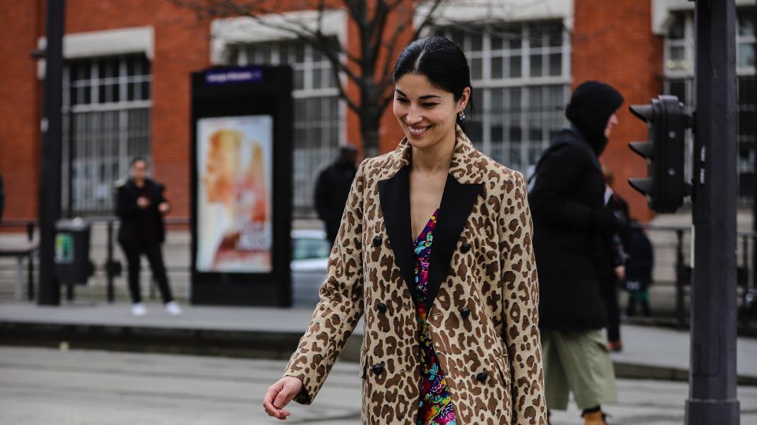 γυναίκα με λεοπάρ παλτό και φόρεμα περπατά στο δρόμο