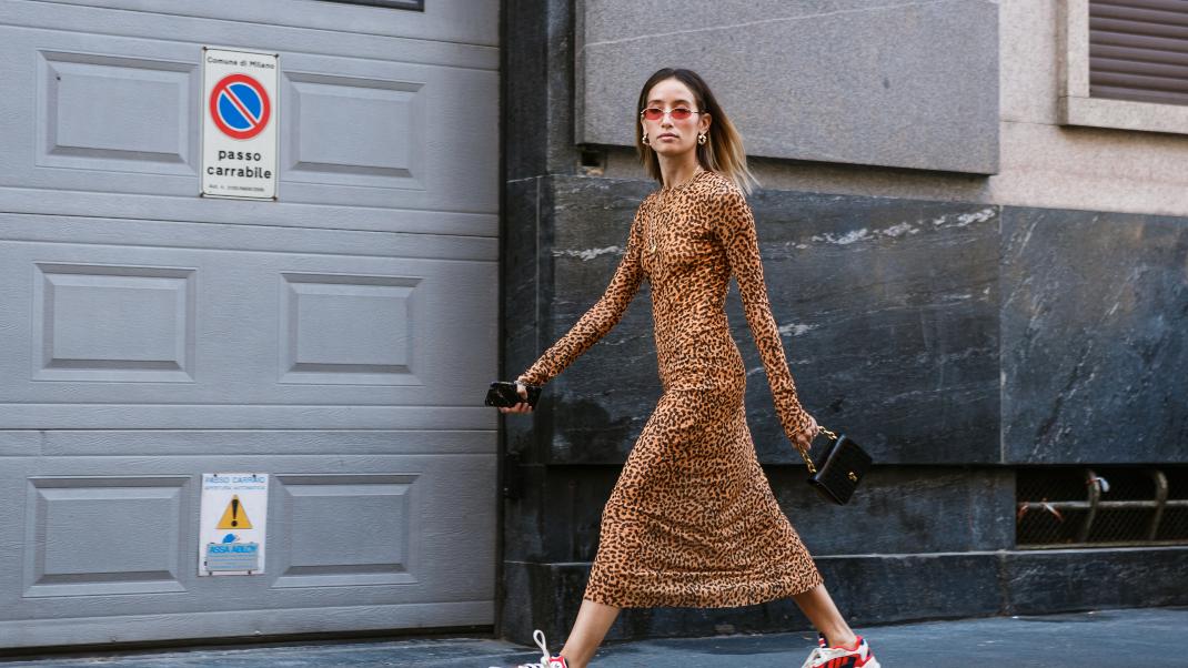 γυναίκα με φόρεμα και sneakers περπατά στο δρόμο