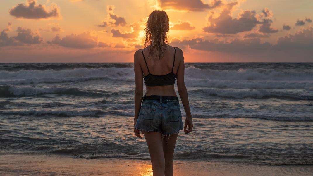 Γυναίκα απολαμβάνει ηλιοβασίλεμα σε παραλία 
