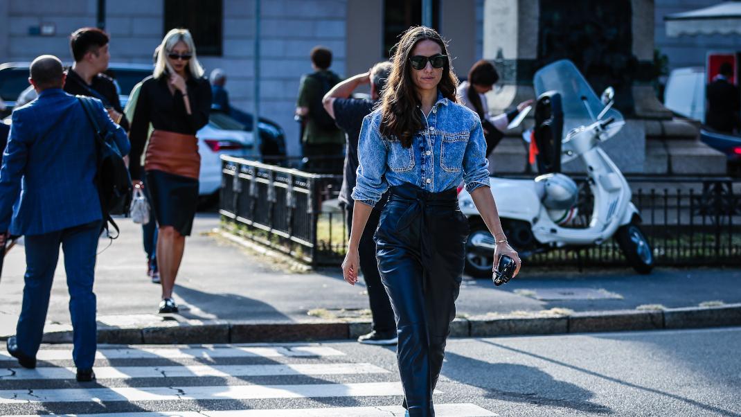 Γυναίκα με τζιν πουκάμισο, δερμάτινο παντελόνι και φλατ περπάτα στον δρόμο