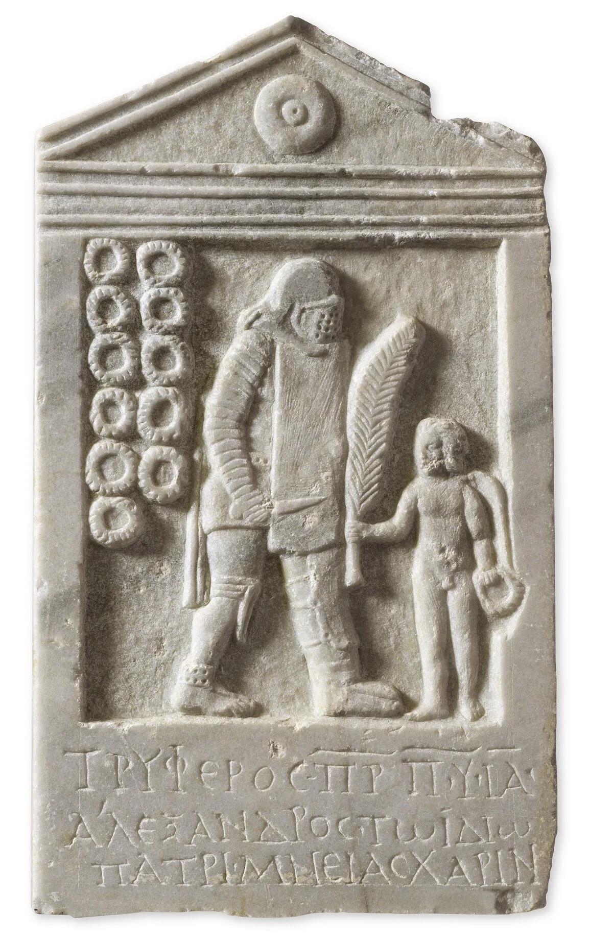  Μαρμάρινη επιτύμβια στήλη με τον μονομάχο Τρύφερο στον τύπο του διώκτη, βαριά οπλισμένο, και έντεκα στεφάνια ως σύμβολα των νικών του. Πάτρα, Βόρειο Νεκροταφείο, 2ος–3ος αι. μ.Χ. 