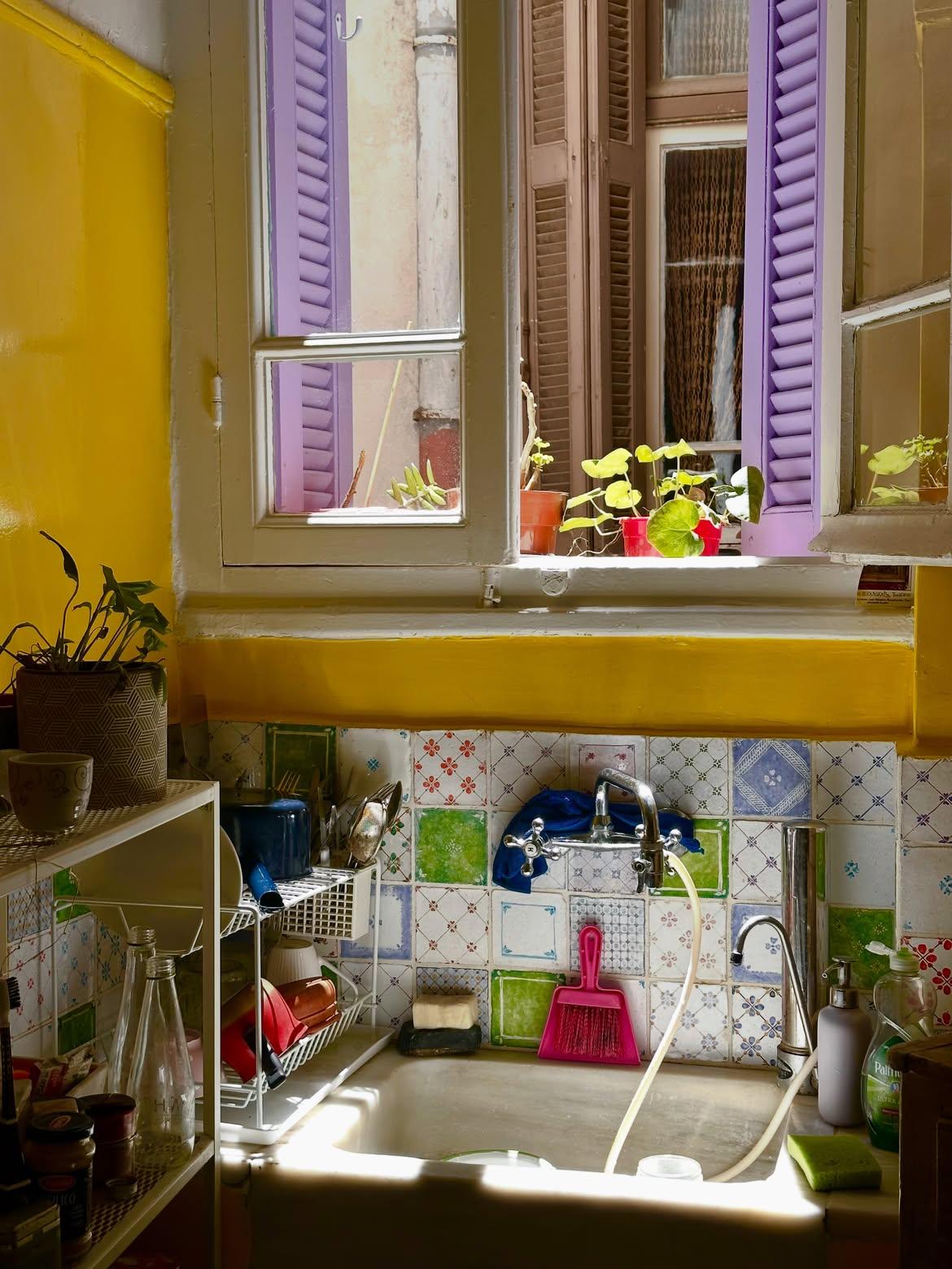 Η κουζίνα ξεχωρίζει με τους κίτρινους τοίχους και τα πολύχρωμα πλακάκια με διαφορετικά μοτίβα.