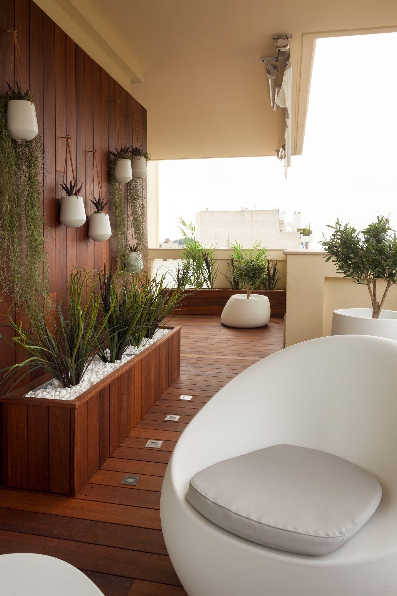 Ο εξωτερικός χώρος φέρνει μια απροσδόκητη τροπική νότα, με ξύλινο πάτωμα, πλούσια φυτά και λευκούς καναπέδες/ Φωτογραφία: Κώστας Μητρόπουλος