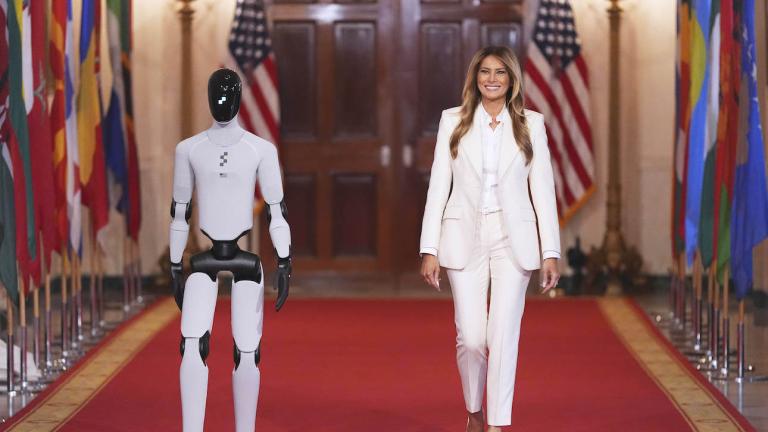 Η Μελάνια Τραμπ με λευκό κοστούμι περπατάει στον λευκό οίκο δίπλα σε ένα ρομπότ