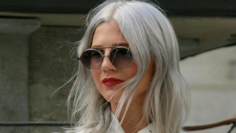 νεαρή γυναίκα με λευκή μπλούζα, μαύρη τσάντα, γυαλιά και γκρίζα μαλλιά