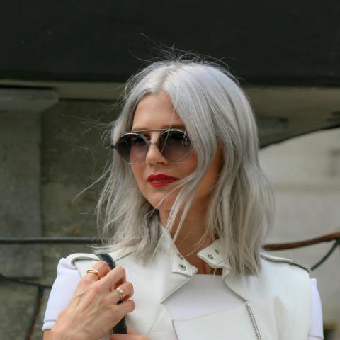 νεαρή γυναίκα με λευκή μπλούζα, μαύρη τσάντα, γυαλιά και γκρίζα μαλλιά